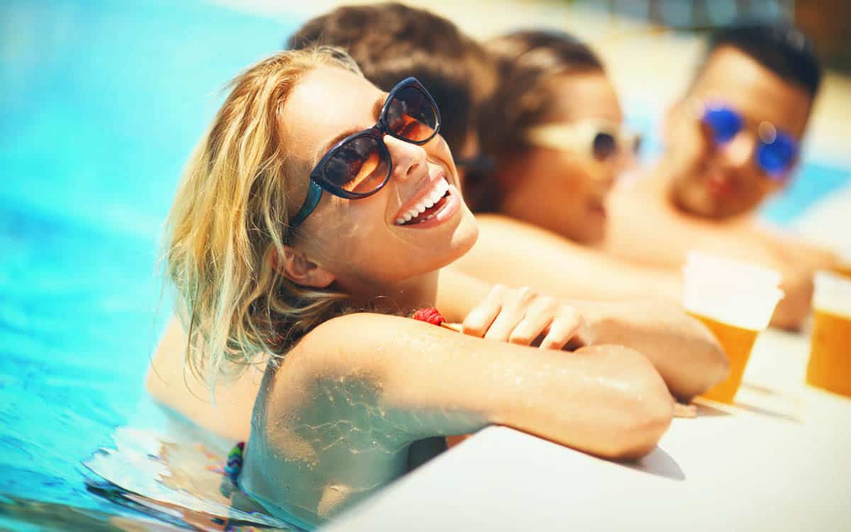 Friends laughing and enjoying drinks poolside capture the fun, relaxing spirit of Northern Colorado Pools in summer.